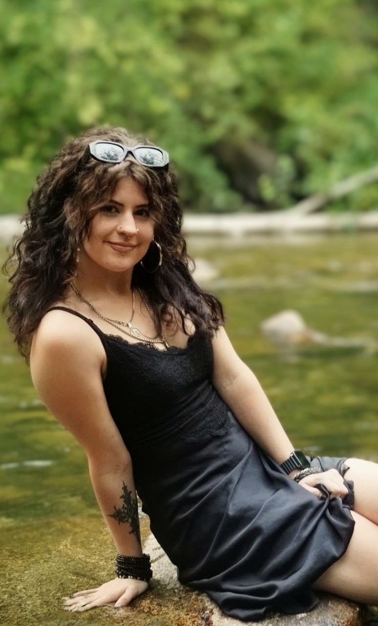 Desirée sitting beside a river in a black dress